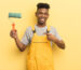 black afro young man smiling cheerfully, feeling happy and pointing to the side. housekeeper painting home